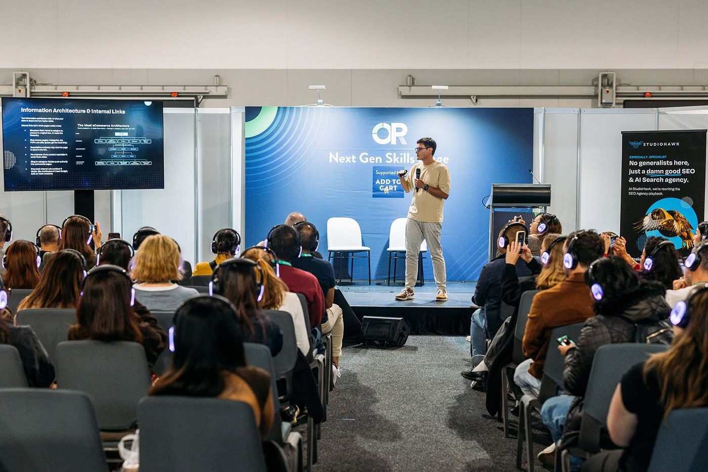 Lawrence Hitches presenting How to do an AI SEO Audit for eCommerce on the Next Gen Skills Stage at Online Retailer 2026, with the ideal ecommerce architecture slide on screen and a full audience